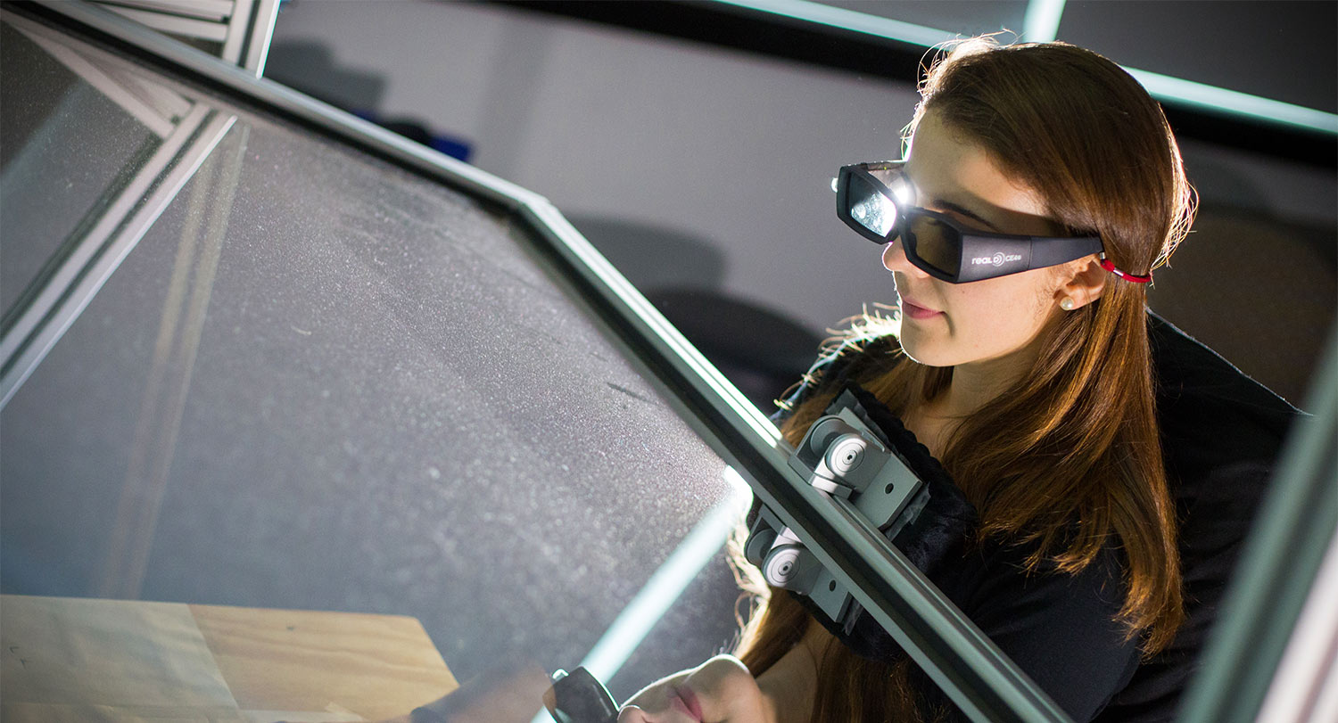 Student waring 3D goggles stares through a glass plane during an experiment.