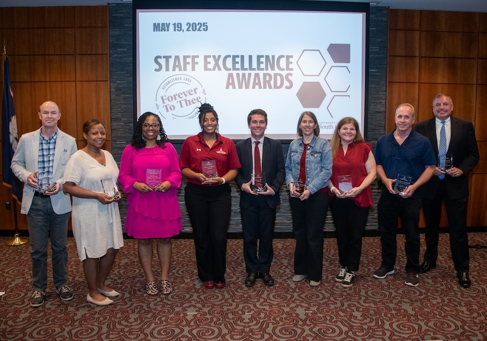 group of people standing in a line smiling and holding glass awards